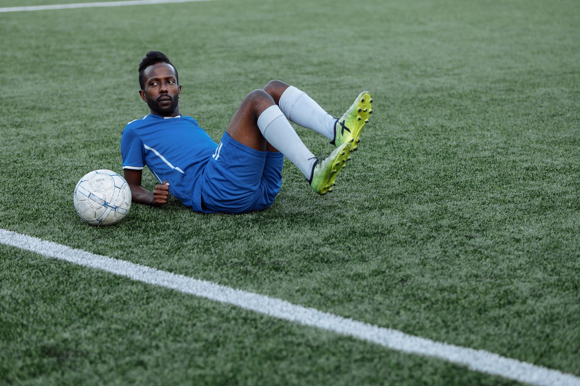 Un joueur de football en maillot bleu allongé sur le terrain avec un ballon à ses côtés.